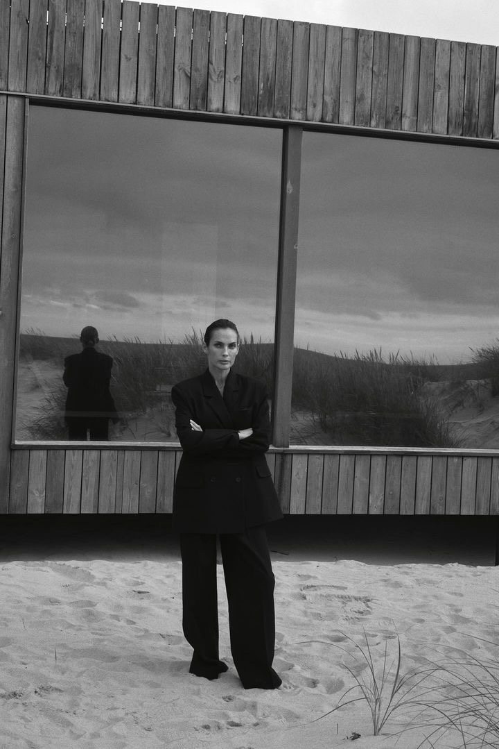 Natalia Boykova, full length in a black suit outside a dune house